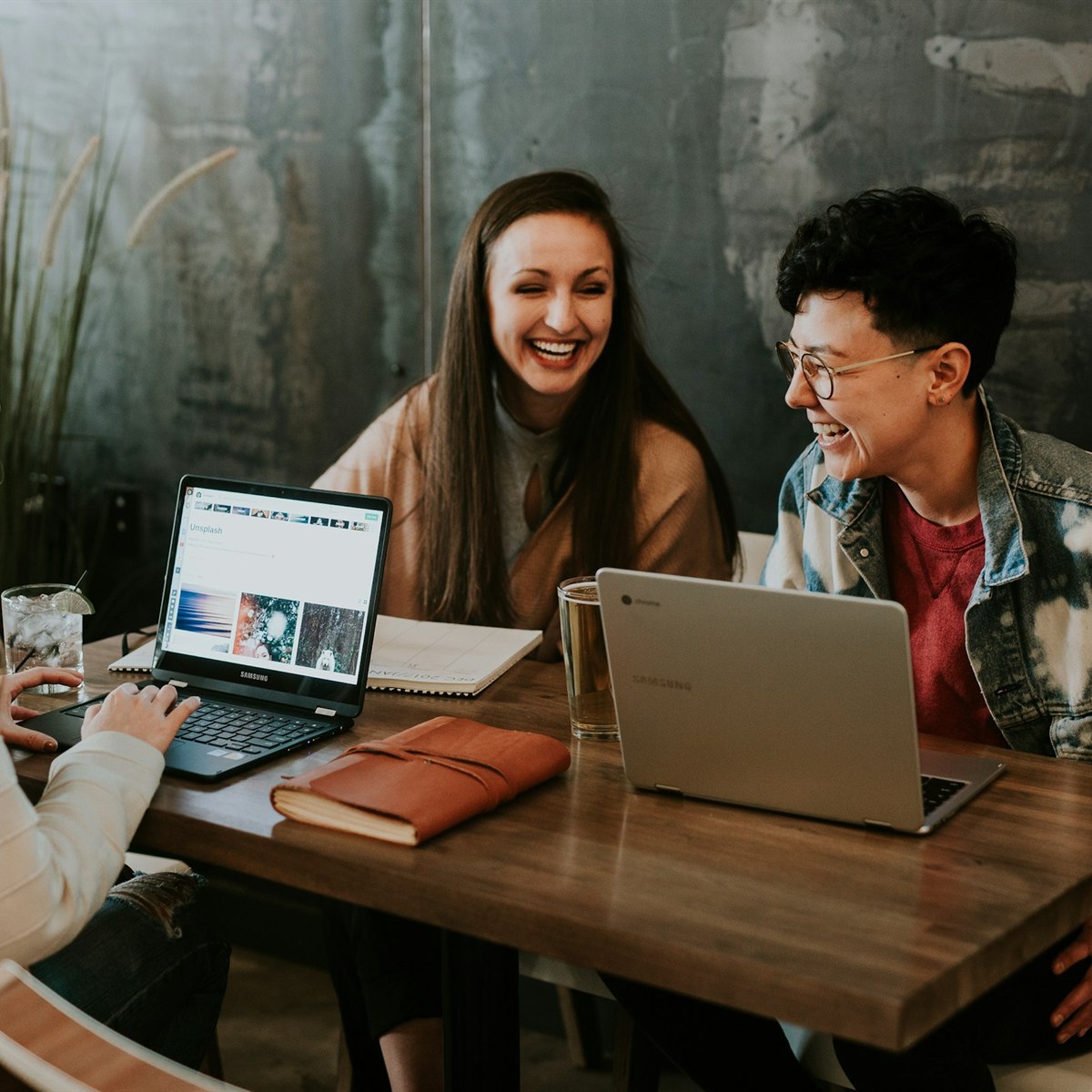 Three colleagues laughing together over their laptops
