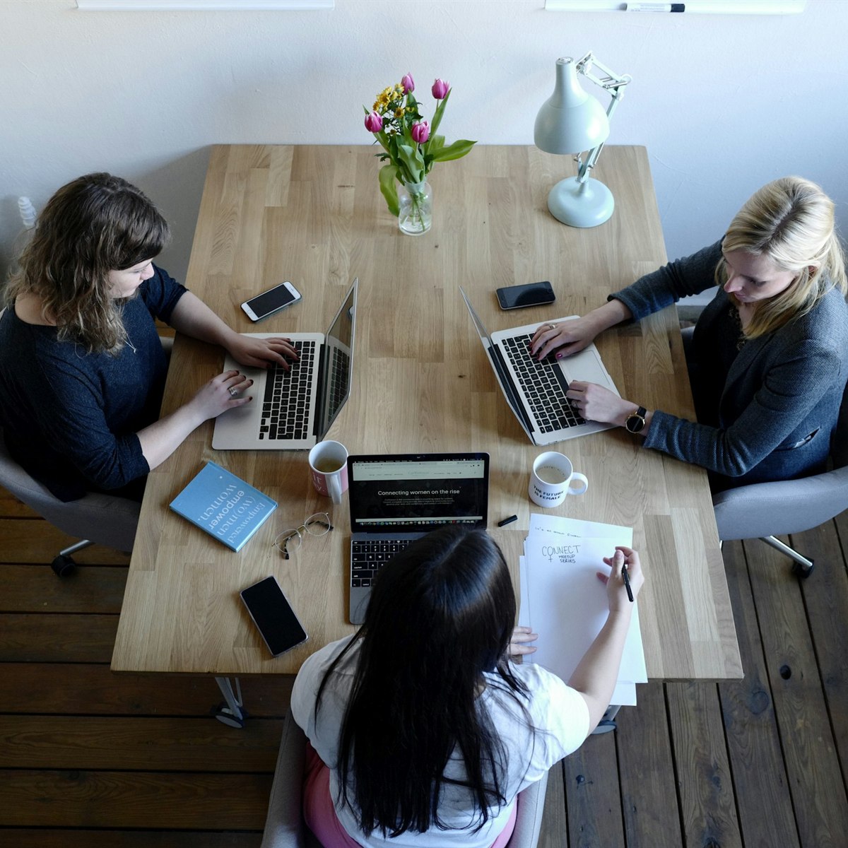 Three women working on laptops around a wooden table